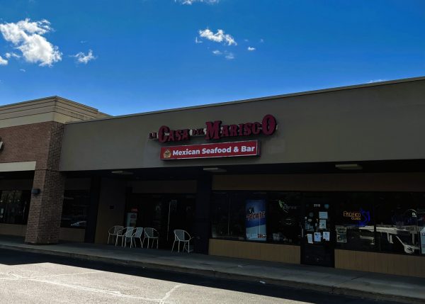 A storefront for "La Casa Del Marisco" Mexican Seafood & Bar, with a sign above and four white chairs outside under an overhang.