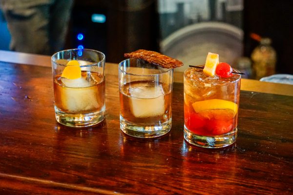 Three glasses of iced drinks on a wooden bar.