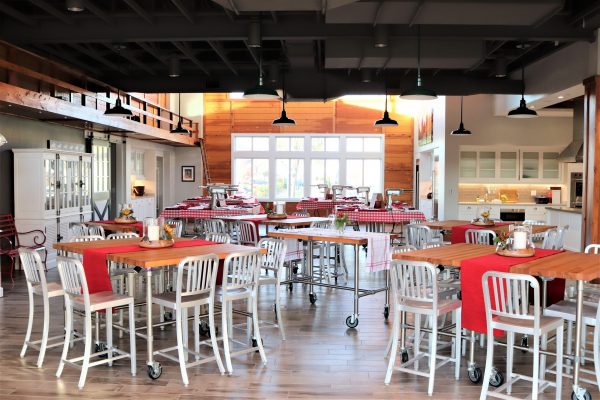 Spacious dining area at Frostwood Farms, featuring high tables and white chairs, red table runners, checkered tablecloths, and bright natural light from large windows—perfect for your next dining venue.