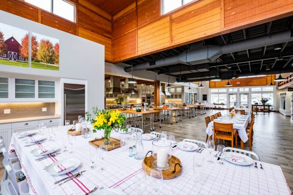 A spacious, modern dining area at Frostwood Farms features large wooden tables set for dining, an open kitchen in the background, and natural light streaming through expansive windows—perfect for your next venue.