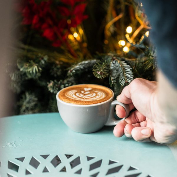 A person holding a cup of coffee in front of a christmas tree.