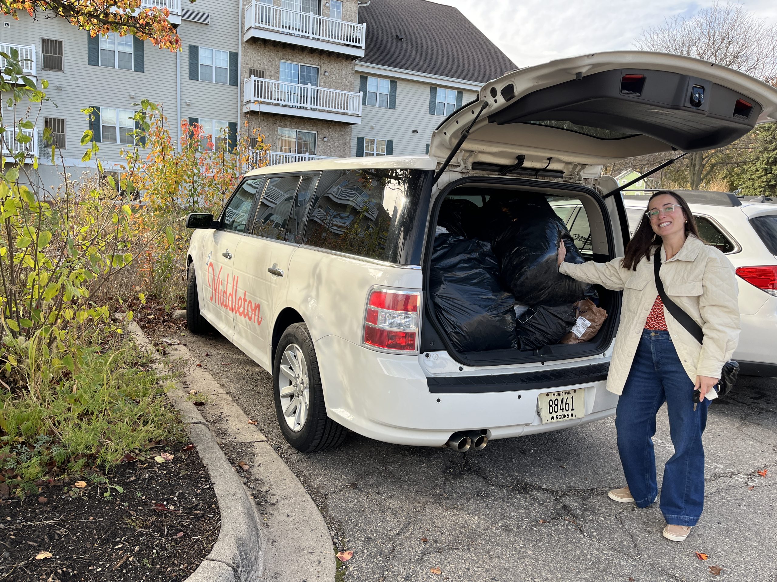 A person stands next to an open vehicle trunk filled with large black bags in a residential area parking lot. The vehicle has "Salvation" written on the side.