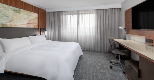 A hotel room with a bed, desk and tv.