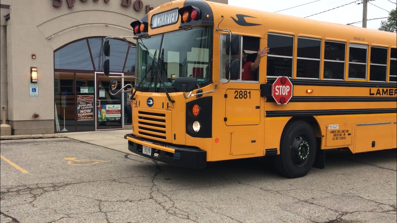 A yellow school bus with an extended stop sign is parked outside a building. A person inside is waving, and the bus displays the number 2881, ready to begin its Spring itinerary.