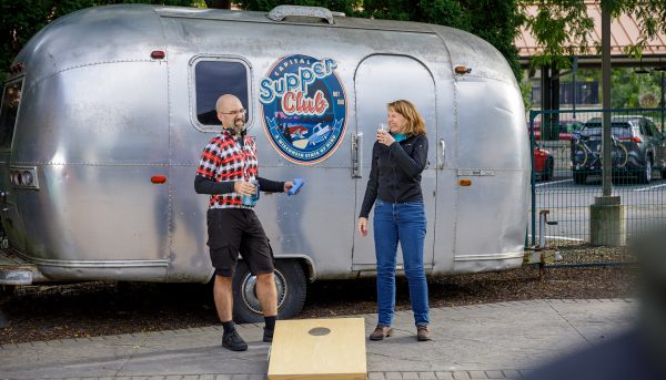 a man and a woman standing in front of a silver trailer.