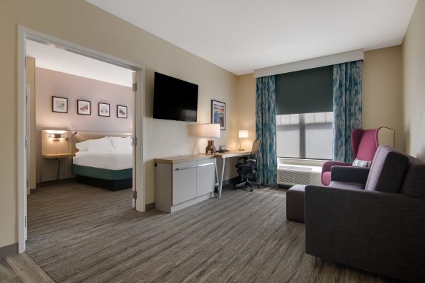 A hotel room with a bed, desk, chair and tv.
