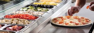 a person putting toppings on a pizza in a display case