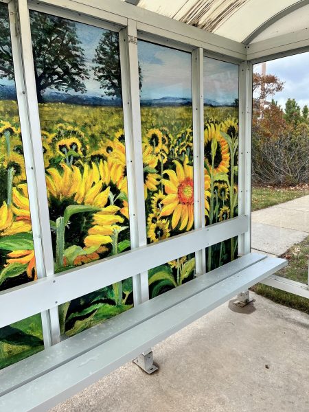 Bus stop shelter featuring a mural of vibrant sunflowers and trees under a blue sky.