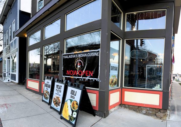 Street view of Thali Ava's Indian Cuisine with "Now Open" banner and menu signs for meat platter and idli dosa outside.
